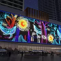 Night View Of Large LED Screen With Colorful Marine Life Sun Trees Tall Buildings Pedestrians