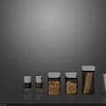 Clear Glass Kitchen Storage Jars With Silver Lids Holding Spices And Dried Ingredients On Black Surface