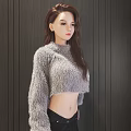 Woman In Gray Fuzzy Cropped Sweater And Black Pants Against Dark Vertical Striped Wall