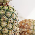 Two Pineapples One Standing and One Lying on Wooden Table with Marble Background and Sunlight