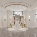 Elegant Bridal Shop Displaying Wedding Dresses On Central Stand With Floral Decor And Bright Lights