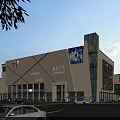 Modern Commercial Complex With Large Digital Display And Surrounding Vehicles Pedestrians Greenery