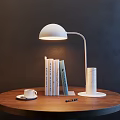 White Curved Arm Table Lamp Illuminating Reading Books with Coffee Cup on Wooden Round Table