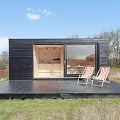 Black Detached House With Large Glass Windows And Lit Interior In Natural Surroundings