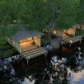 Wooden Pergola With Thatched Roof Illuminated By Waterfront Trees And Water Reflection At Night
