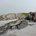 Scenic Beach Landscape With Gray Sand Rocky Outcrops And Green Grass Hills