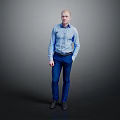 Man In Blue Shirt And Blue Pants Standing With Hands In Pockets Against Gray Background