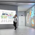 Public Wall With Orange Illuminated Hello Graphic Cartoon Character And Large Screen Showing Map Info