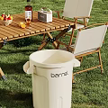 Outdoor White Plastic Barrel Trash Can Near Wooden Table With Foldable Chairs On Grass