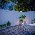 Serene Nighttime Outdoor Space With White Fence Stone Patio Green Plants And Striped Chair