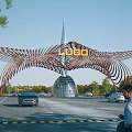 Modern Wing Shaped Metal Entrance Gate With Top LOGO Surrounded By Cars And Pedestrians