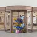 Activity Entrance With Brass Revolving Door Glass Panels And Decorative Floral Arrangement