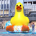 Outdoor Photo Spot with Giant Yellow Inflatable Duck and Colorful Rings Near Modern Buildings