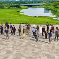Group of People in Paved Plaza With Green Grass Lake Trees and Bridge