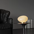 Oval Shaped Cream Colored Table Lamp with Gold Base on Black Table Near Leather Sofa