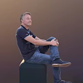 A Man Sitting On A Green Cube Wearing Dark Blue Polo Shirt And Blue Jeans