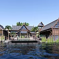 Tropical Wooden Resort Buildings With Gabled Roofs Palm Trees And Calm Waterfront View