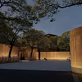Evening View Of Architectural Courtyard With Landscaped Trees Circular Stone Walls And Warm Lighting