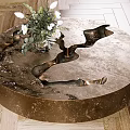 Round Metallic Coffee Table With Sculptural Indents And White Flower Arrangement On Wooden Floor