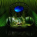 Enchanting Stage Featuring Green Laser Beams Blue Circular Screen Forest Background and Reflective Base