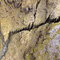 Scenic Mountainous Terrain With Flowing Stream Yellowish Green Textured Slopes And Visible Cracks