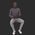Man Sitting Against Black Background Wearing Gray Sweater Light Gray Pants And White Sneakers