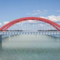 Modern Red Arch Bridge Spanning Calm River Under Bright Blue Sky With Soft White Clouds
