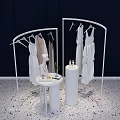 White Display Racks Hanging White Dresses With Round Table Cylindrical Stand Dark Background Pebble Floor