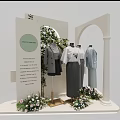 Mannequins Wearing Simple Classic Clothes In Display Area With Green Plants And Flower Decorations