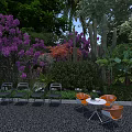 Garden Landscape With Purple Flowering Plants Lush Greenery Outdoor Chairs And Round Table