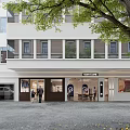 Modern Storefront Facade Design With Glass Doors Wooden Accents Trees And Pedestrians