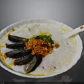 Savory Congee Topped with Century Egg Green Onions Chili Flakes in White Bowl with Spoon