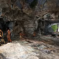 Natural Cave Interior Featuring Rock Formations Ancient Humans Campfire Sunlight Through Entrance And Green Plants
