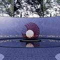 Red Spherical Sculpture With Silver Center In Circular Pool Surrounded By Trees And Gray Wall
