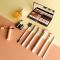 Perfume And Cosmetics Collection With Eyeshadow Palette Lipstick Brushes And Mascara On Soft Color Background