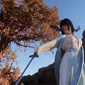 Woman In Traditional Robe Holding Sword Near Ancient Tree And Rocky Mountains Under Blue Sky