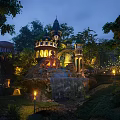 Enchanting Night Scenery with Illuminated Castle Waterfall Wooden Bridge and Lush Trees Garden Lights