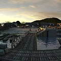 Riverside Ancient Architecture Scene With Wooden Plank Walkway Boats And Distant Hills At Sunset
