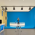 Professional Broadcasting Studio Setup With Blue Backdrop Presenter Desk Camera Tripod Lighting And Control Monitor