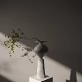Gray Vase with Branch and Green Leaves Against Light Colored Wall with Sunlight Shadow