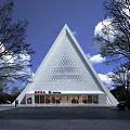 White Triangle Shaped Building With Hollowed Out Design And Red Signage Surrounded By Trees