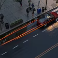 People walking on sidewalk near red car at crosswalk with wet road surface and street lamps