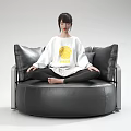 Woman Sitting Cross Legged On Black Leather Round Sofa Wearing White Top With Yellow Pattern