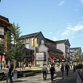 Traditional Style Commercial Street With Walking Pedestrians Storefronts And Lush Green Trees