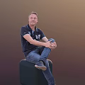 A Man Sitting On A Green Cube Wearing Dark Blue Polo Shirt And Blue Jeans