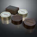 Round Metal Cans With Gold Lids And Brown Box On Dark Surface