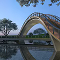 Modern Arched Landscape Bridge With Metal Railings Over Water And Tree Reflections