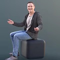 Smiling Man Sitting On Black Cube Wearing Gray Cardigan And Blue Jeans