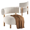 Light Beige Upholstered Leisure Chair With Curved Backrest Wooden Legs And Brown Knitted Blanket