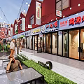 Vibrant Commercial Street With Red Roof Buildings Shops Outdoor Seating Green Plants And String Lights